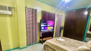 Une chambre à coucher avec un lit, une télévision, des rideaux et un appareil de climatisation.