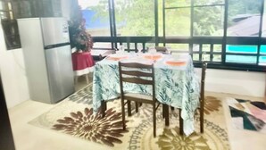Un coin repas avec une table dressée pour quatre personnes, un réfrigérateur et une vue sur la verdure environnante.