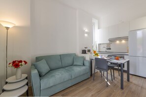 Une cuisine moderne avec des meubles blancs, une table à manger avec des chaises, un canapé et un lampadaire.