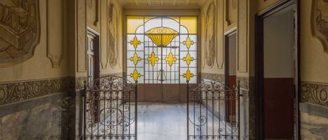 A hallway with a marble floor, ornate wall decorations, and a large window with yellow and white patterns.