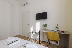 A hotel room with a bed, a desk with a chair, a TV, a small table with a vase and a bottle, and a window. - Pomponazzi, 19 - Two-room apartment in the Bocconi area (Milano)