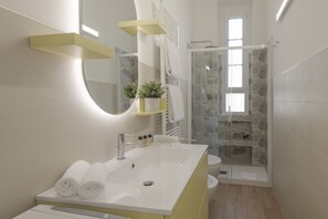 Un baño moderno con lavamanos, espejo y zona de ducha blanca.