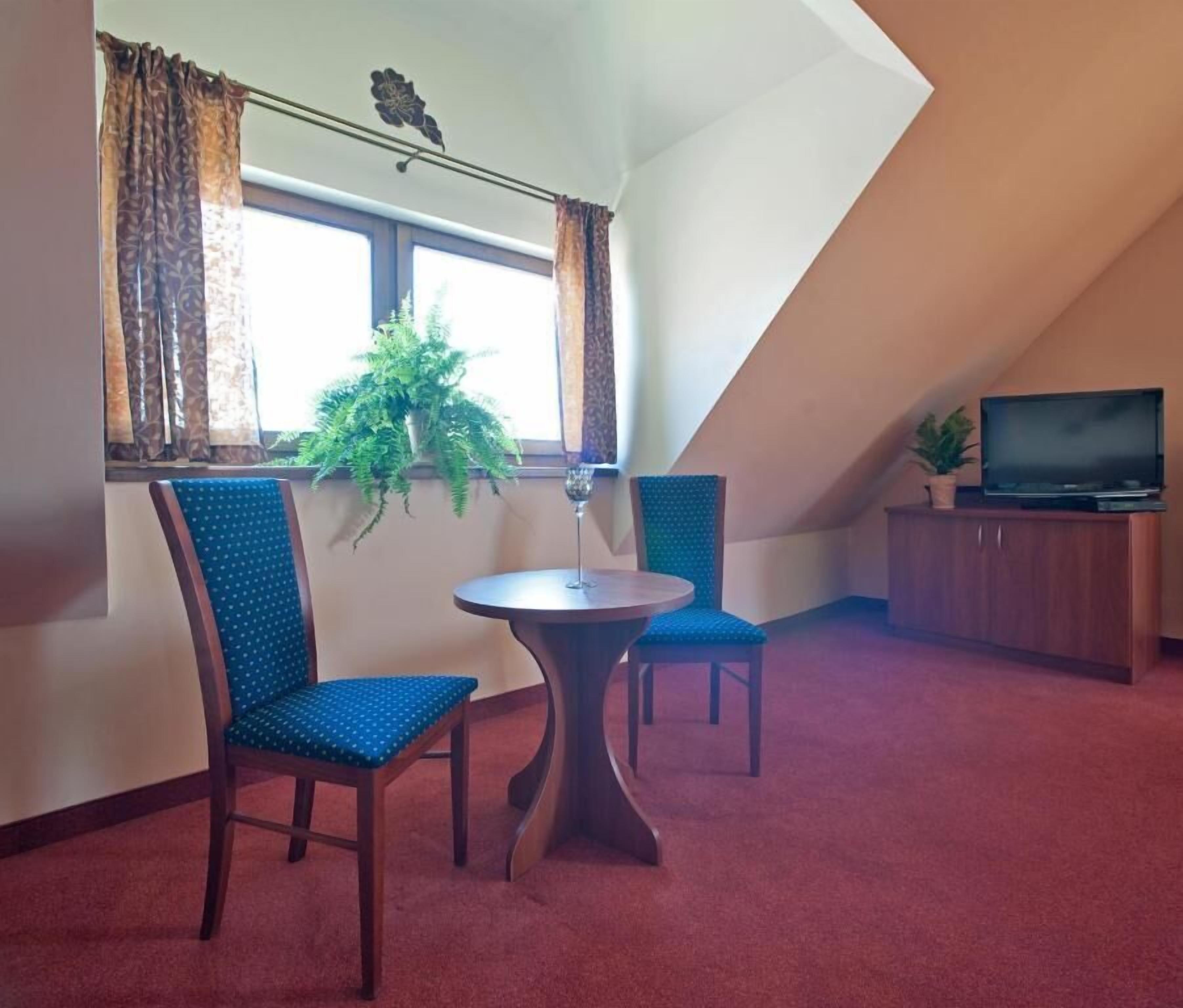 A room with a dining table and two chairs, a TV on a cabinet, and a window with curtains.