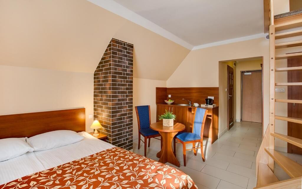 A hotel room with a bed, a small table with chairs, a brick fireplace, and a wooden staircase.