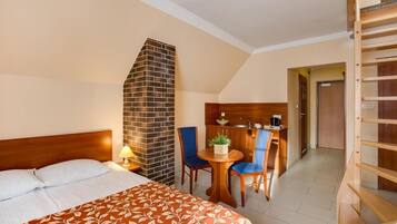 A hotel room with a bed, a small table with chairs, a brick fireplace, and a wooden staircase.