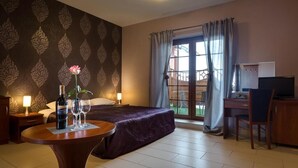 Habitación de hotel con cama, escritorio, silla, mesa con una botella y vasos, y ventana con cortinas.