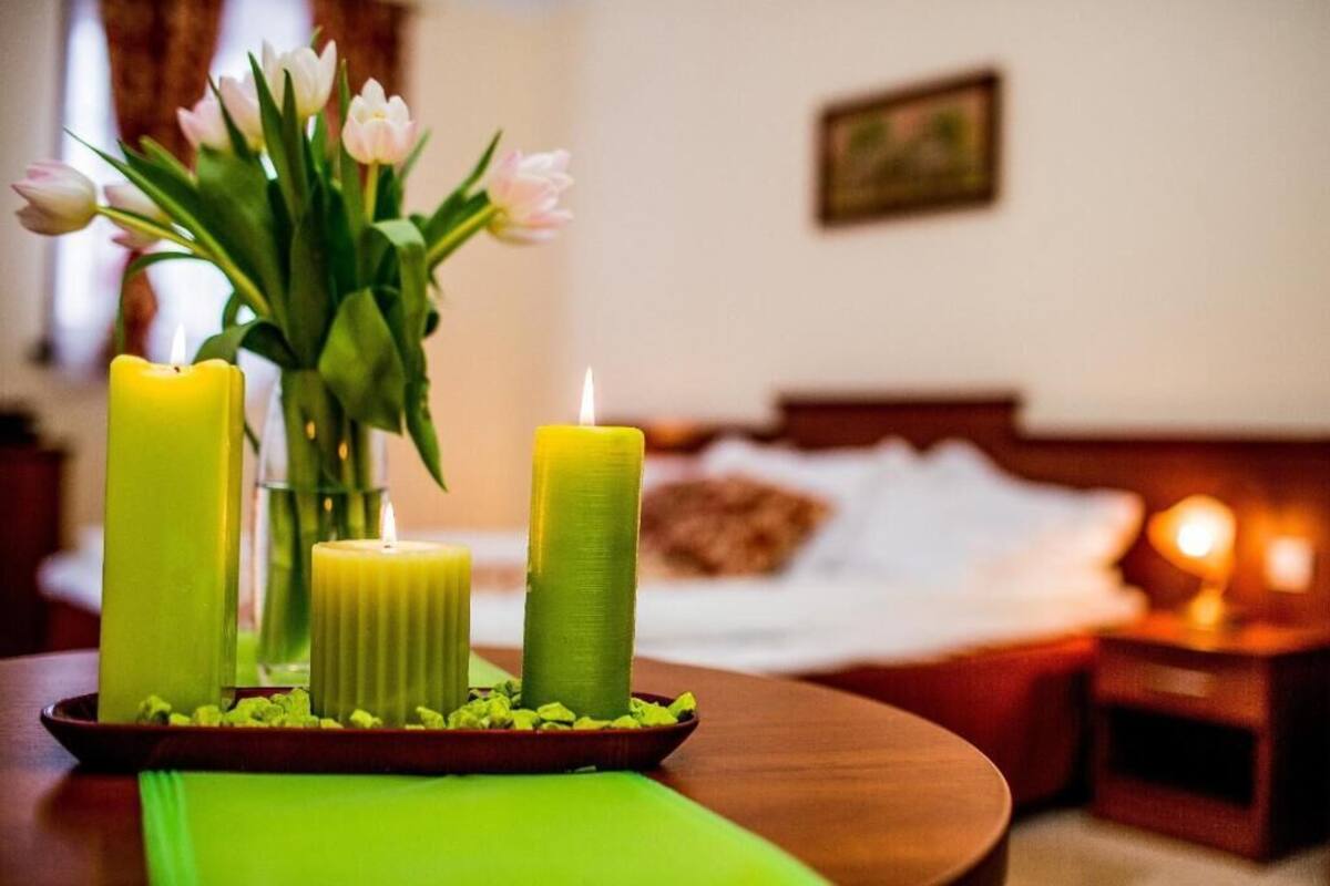 A room with a bed, a bedside table with a candle, and a vase with flowers.