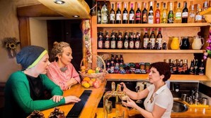 Zona de bar con un cantinero, estantes llenos de botellas de licor y una cesta de frutas.