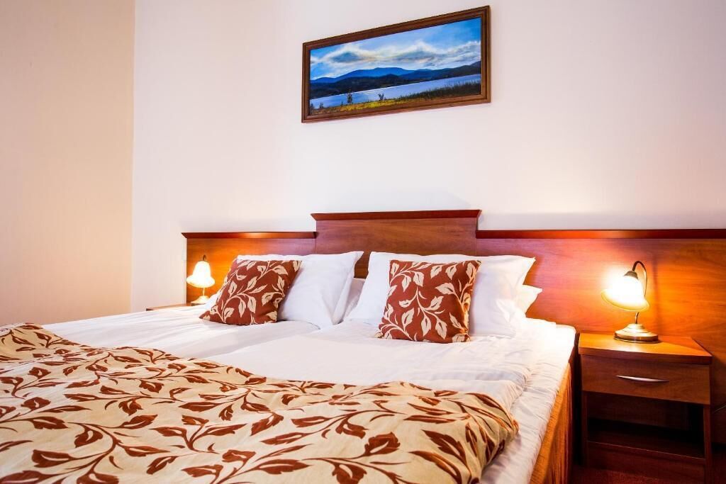 A double bed with a patterned bedspread, two bedside lamps, a nightstand, and a framed picture on the wall.