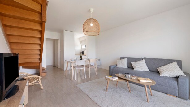 Una sala moderna con un sofá gris, una mesa de centro de madera y un televisor.