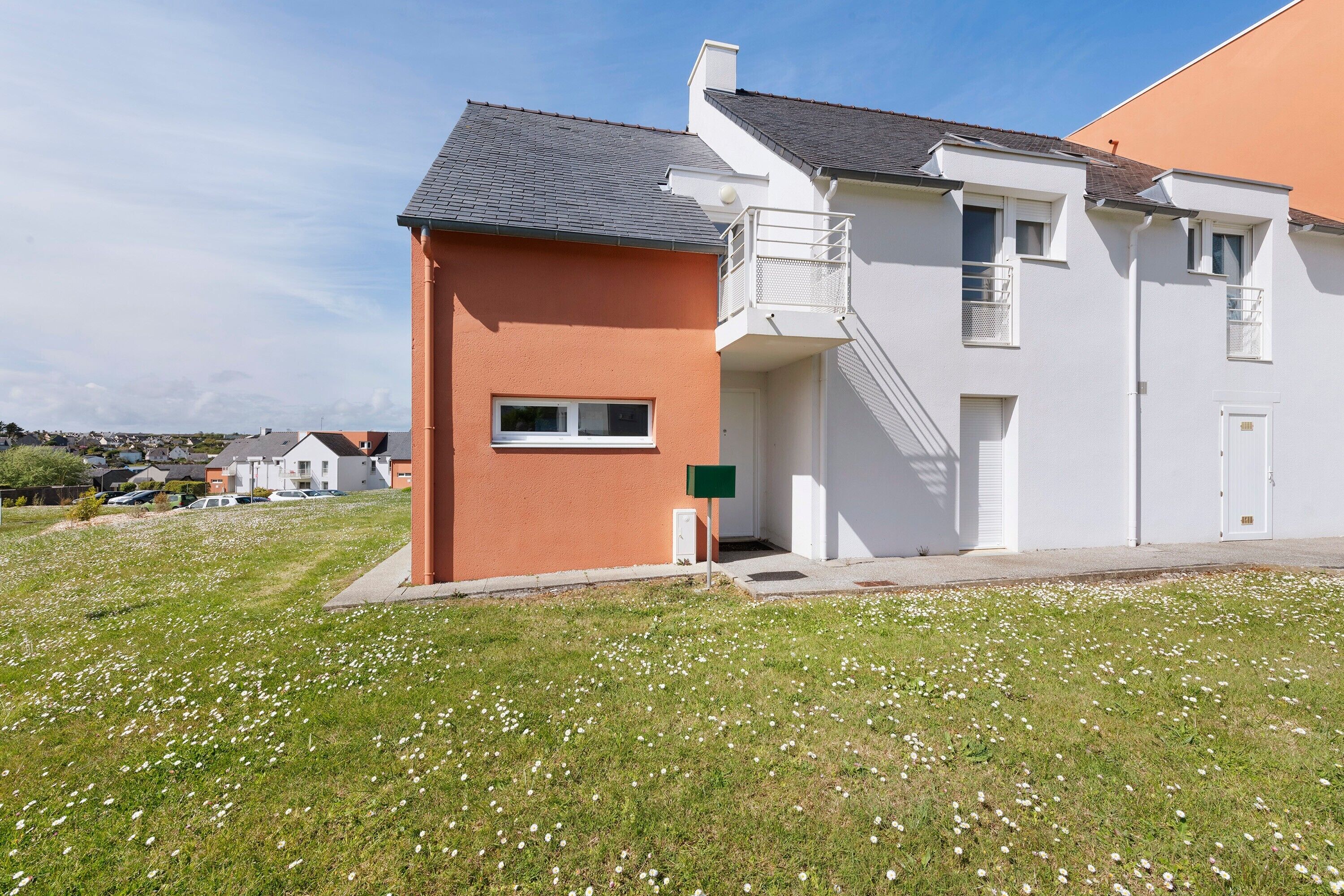 A residential building with a red and white facade, a balcony, and a grassy lawn.