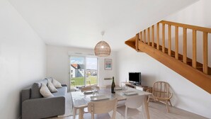 Una sala de estar moderna con sofá, mesa de comedor, sillas, televisor y una escalera.