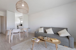 En moderne stue med en grå sofa, hvide puder, et træbord og et spiseområde med et hvidt bord og stole.