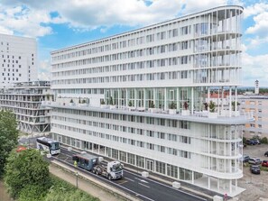 A modern multi-story building with a curved facade, large windows, and a flat roof. - Coliving by UTDM (Huningue)