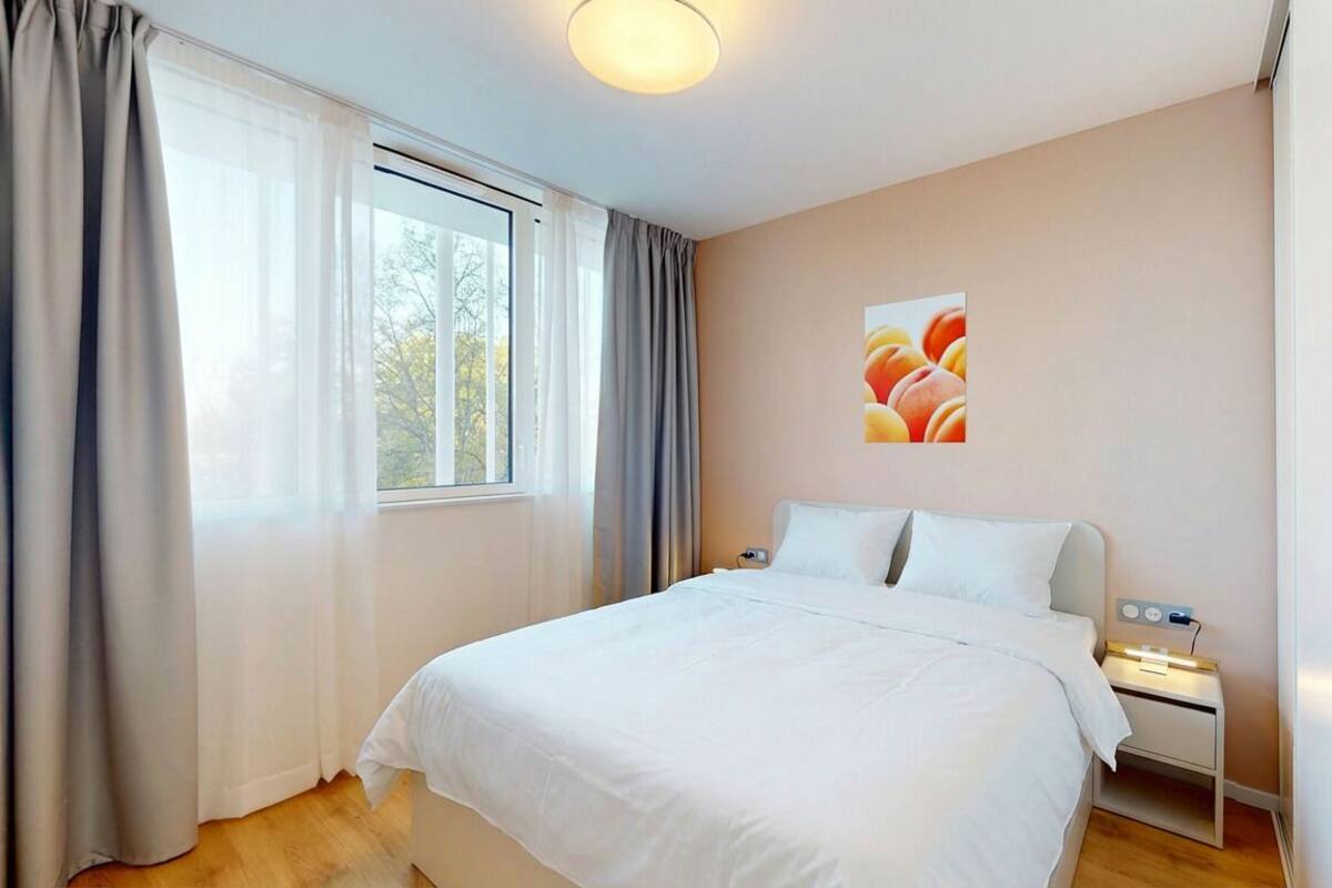 A bedroom with a bed, bedside tables, a window with curtains, and a wall-mounted artwork.