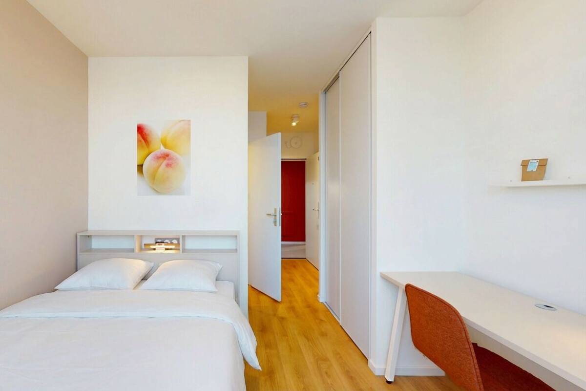 A modern hotel room with a bed, a desk, and a wall-mounted painting.