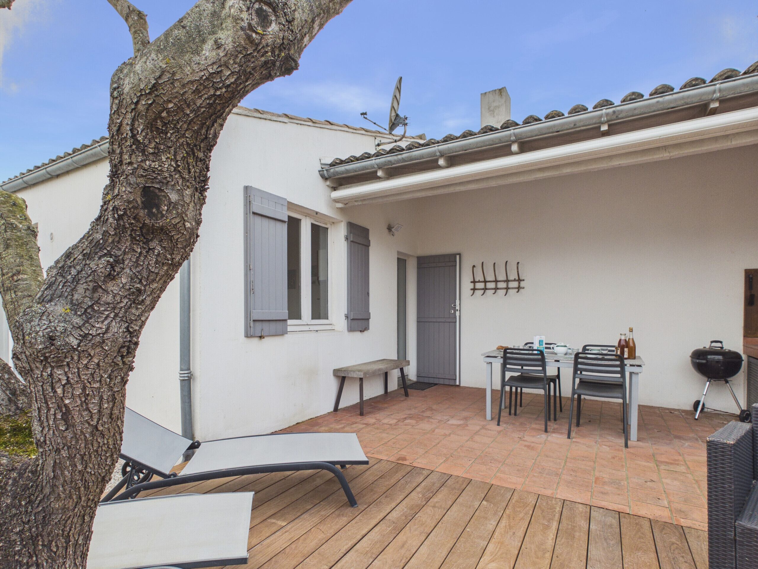 A patio with a table and chairs, a bench, a wall-mounted rack, and a tree.