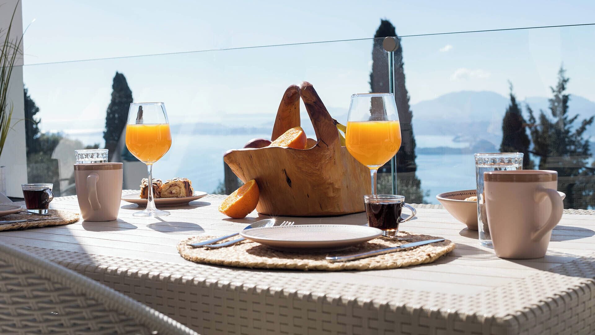 A breakfast setup with bread, juice, and coffee on a table with a view.
