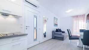 Eine moderne Küche mit integrierten Geräten, ein Essbereich mit Tisch und Stühlen, ein graues Sofa und ein Gemälde eines Segelboots an der Wand.