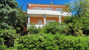 Ein zweistöckiges Gebäude mit einem Balkon, umgeben von üppiger Vegetation.
