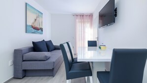 Ein modernes Wohnzimmer mit einer Couch, Sesseln, einem Esstisch, einem Flachbildfernseher und einem Gemälde eines Segelboots.