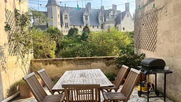 Une terrasse avec une table et des chaises en bois, un barbecue et une vue sur un château.