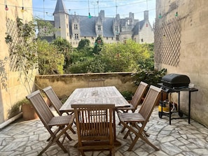 Een terras met een houten tafel en stoelen, een barbecue en uitzicht op een kasteel.