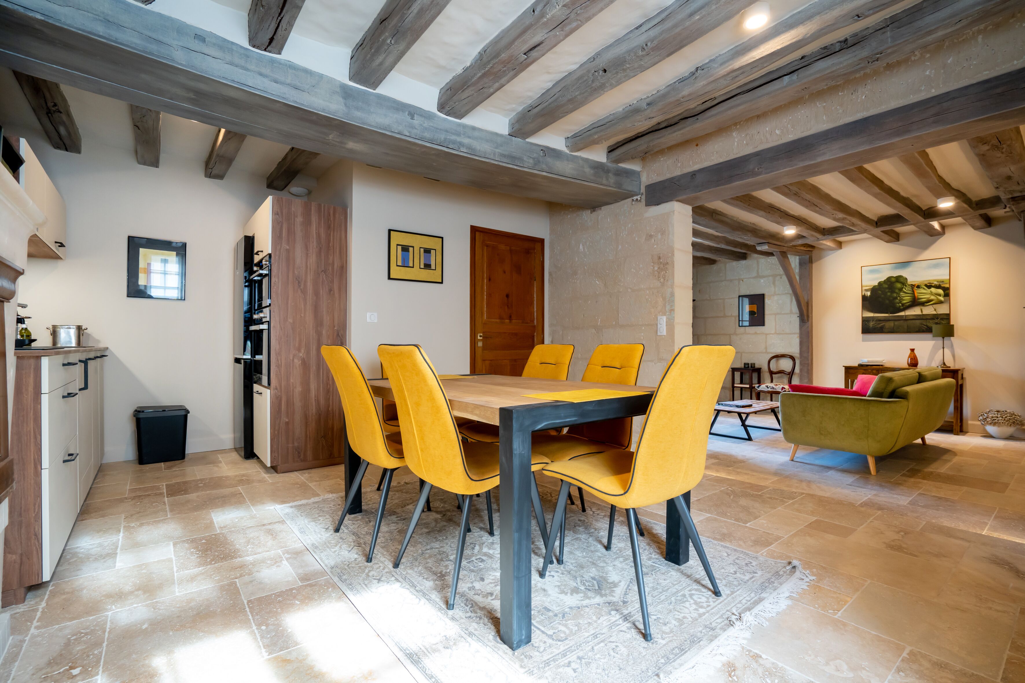 Ein Essbereich mit einem Holztisch und gelben Stühlen, eine Küche mit weißen Schränken und eine Wohnbereich mit einem grünen Sofa.