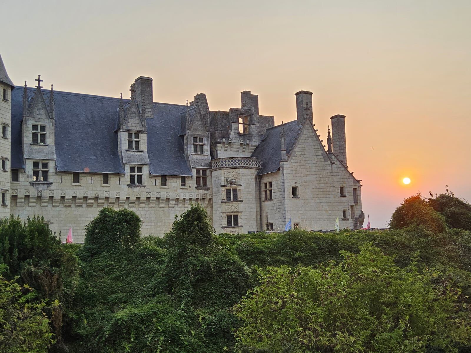 A historic building with multiple towers and a prominent central tower, surrounded by lush greenery.