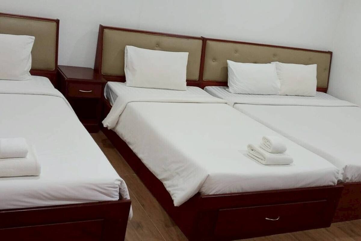 A hotel room with three single beds, each with a wooden headboard and white bedding.
