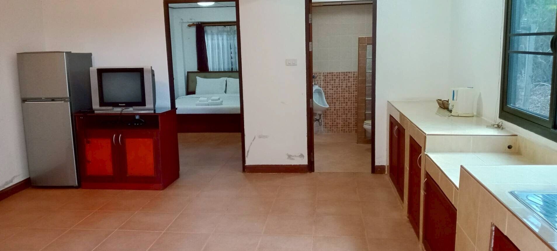 A room with a bed, a television, a refrigerator, a sink, and a window.
