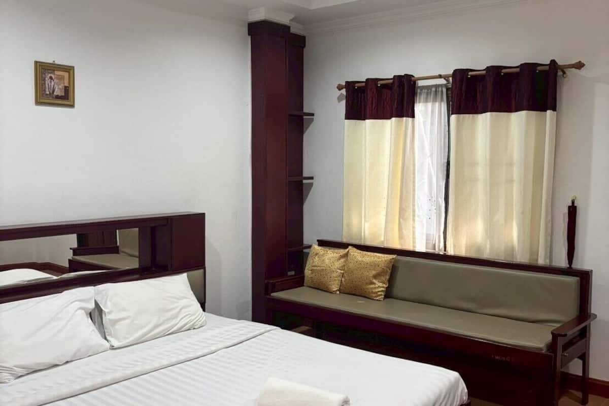 A hotel room with a large bed, a sofa, a wooden cabinet, and a picture on the wall.
