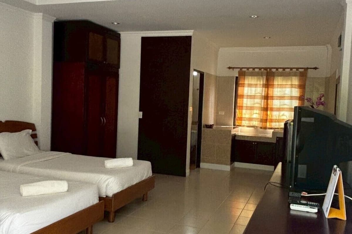 A hotel room with two beds, a desk with a television, and a bathroom visible through an open door.