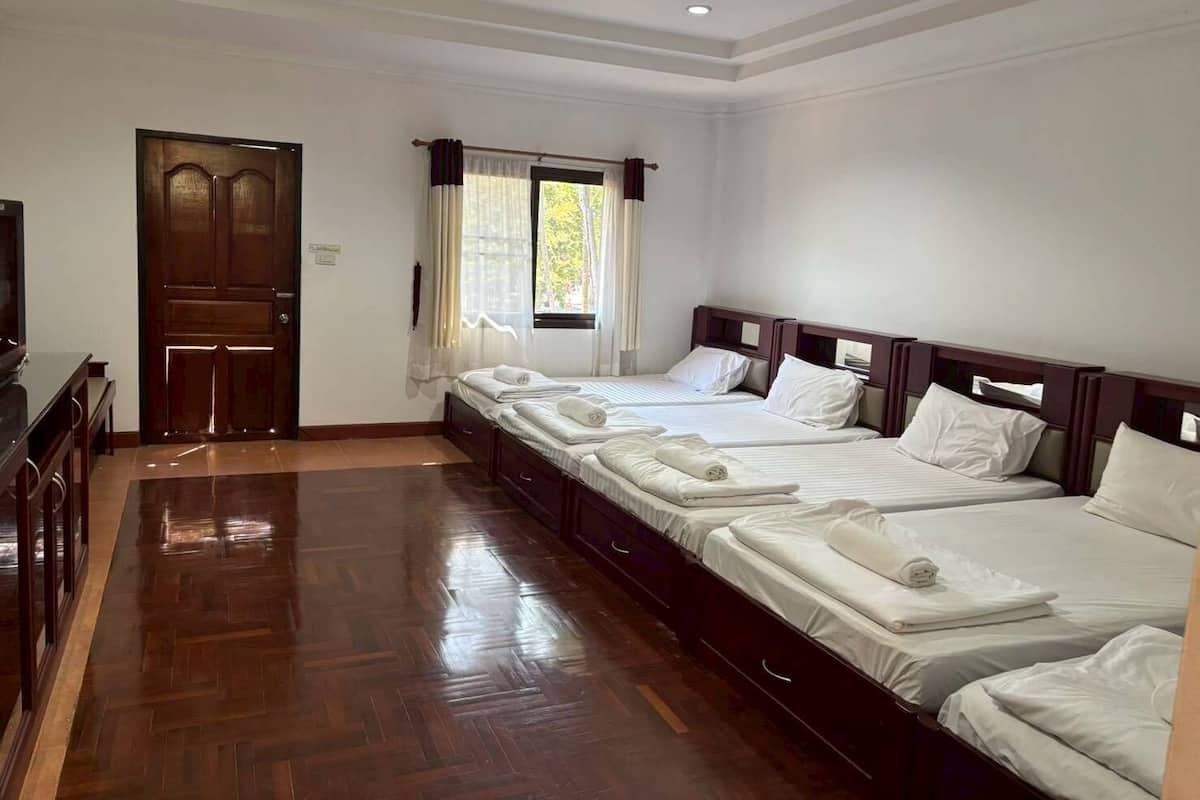 A hotel room with a wooden floor, a large wooden door, a television, and three beds with white bedding.