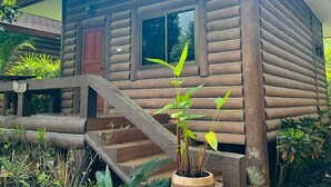 Une cabane en bois avec un escalier menant à l’entrée, entourée de plantes tropicales.