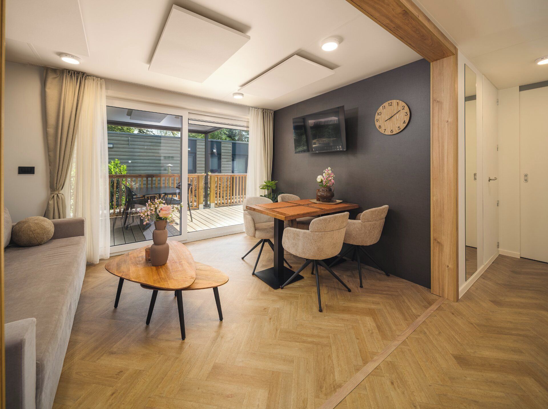Una sala de estar moderna con una mesa de comedor de madera, un sofá y un televisor montado en la pared.