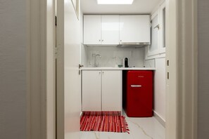 A narrow hallway leading to a compact kitchen with white cabinets, a red refrigerator, and a patterned rug. - Marasli 29 1bdr·Serenity Escape with Jacuzzi (Athens)