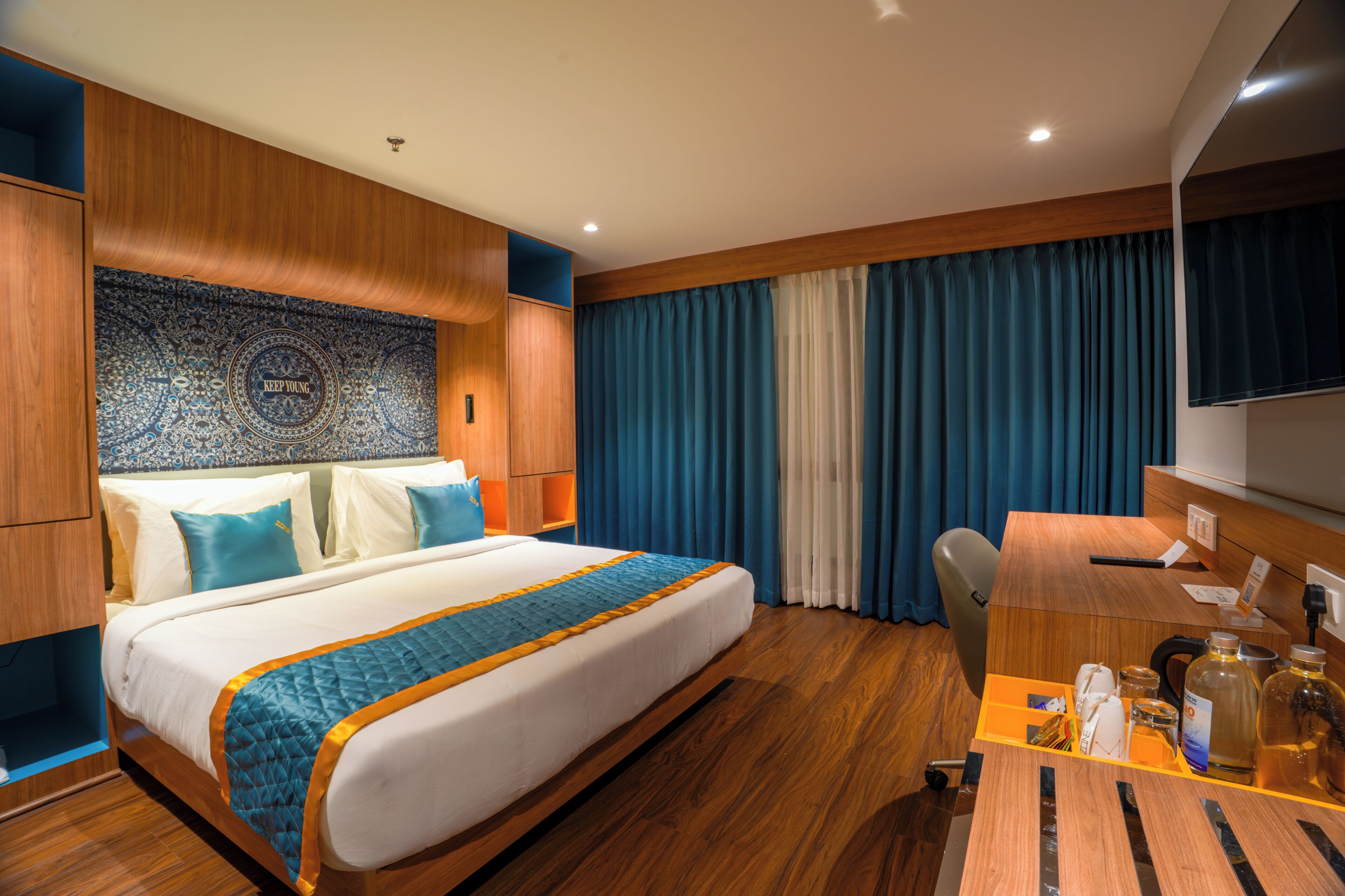 Une chambre d’hôtel avec un grand lit, un bureau avec une chaise, un minibar et une grande fenêtre avec des rideaux.