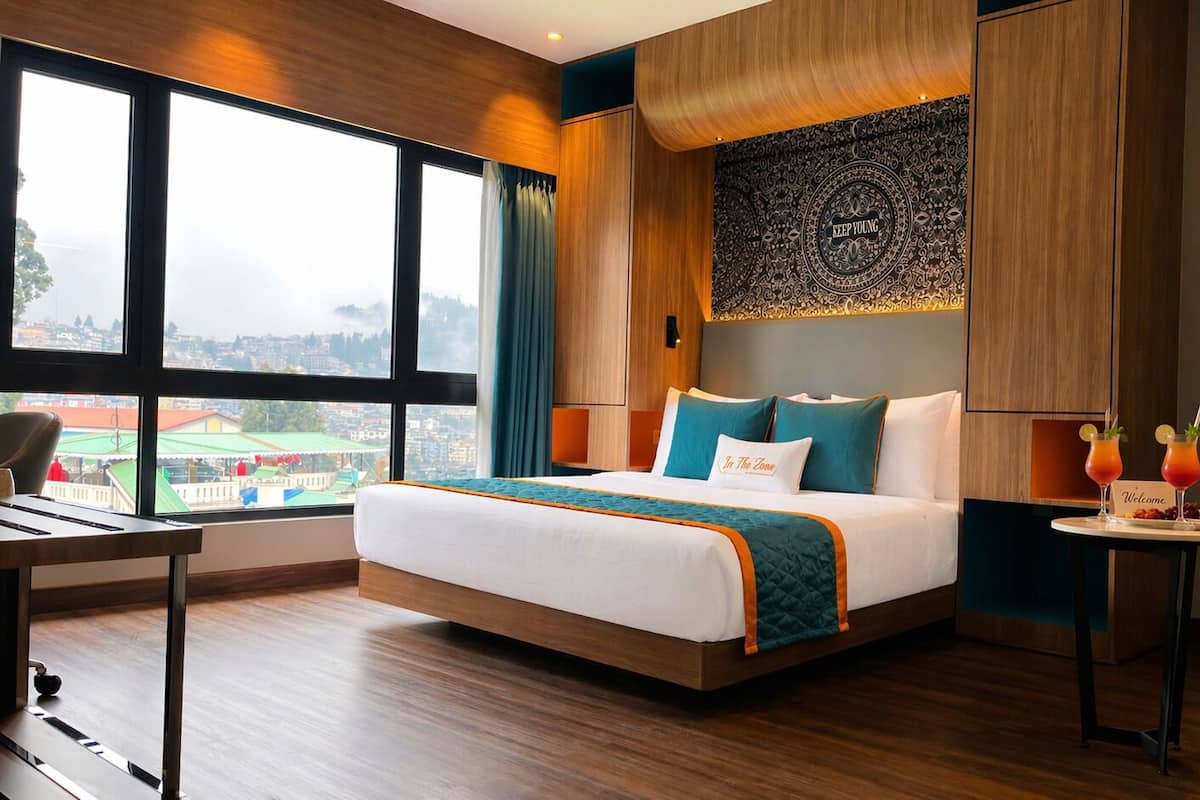 Hotelkamer met een groot bed, bureau, stoel, een klein tafeltje met drankjes en uitzicht op de stad.