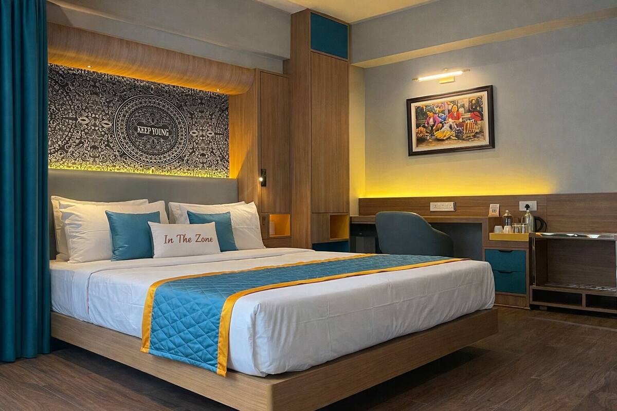 Een hotelkamer met een groot bed, een bureau, een stoel, wandtapijt en een ingelijst schilderij.