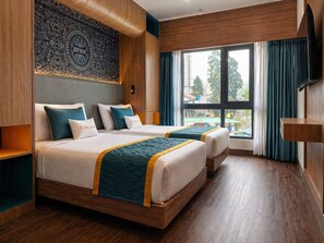 Habitación de hotel con dos camas, un ventanal grande con cortinas, suelo de madera y un tapiz en la pared.