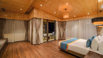 Habitación de hotel con techo de madera, cama con colcha azul y vistas al exterior a través de un ventanal.
