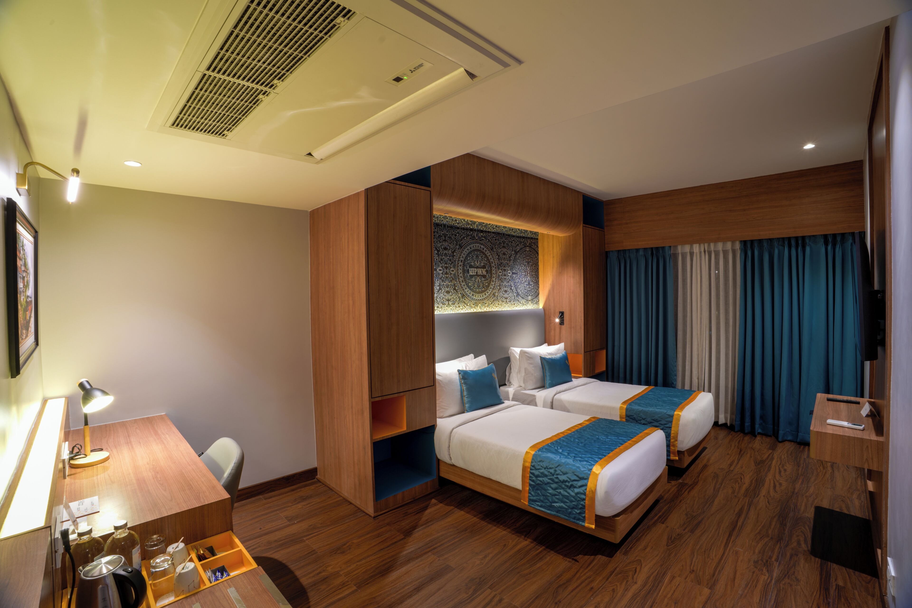 Habitación de hotel con dos camas, un escritorio, una silla, un minibar y un ventanal grande con cortinas.