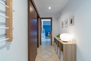 A hallway with a wooden door, a white towel rack, a wall-mounted light, and a small table with a lamp and a bottle. - Le Stanze di Archimede (Siracusa)