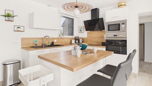 A modern kitchen with a wooden island, white cabinetry, stainless steel appliances, and a hanging light fixture. - House for 6 adults and 3 children – 900m beach (La Forêt-Fouesnant)