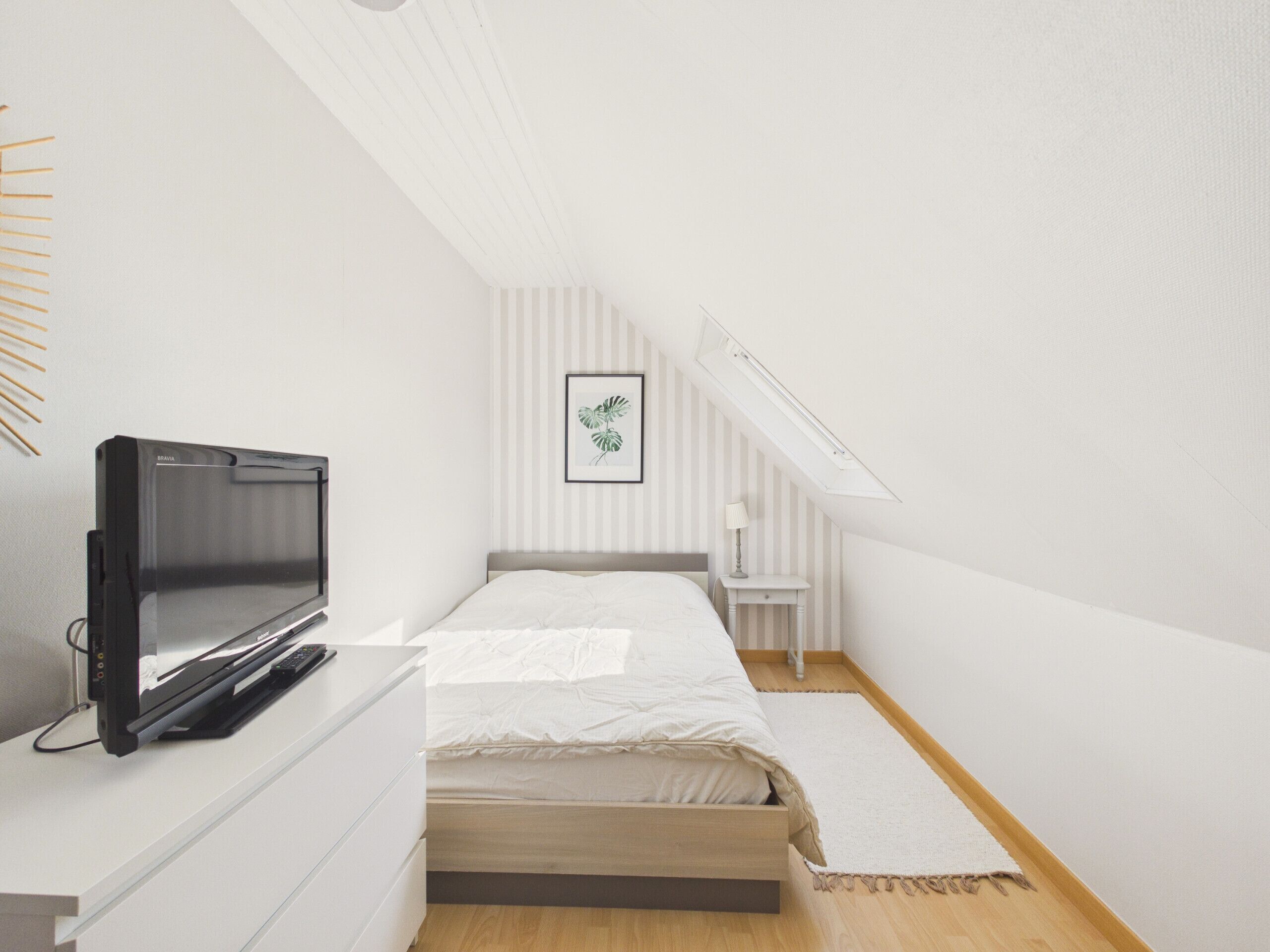 Een slaapkamer met een bed, een televisie, een bureau, een lamp en een raam.