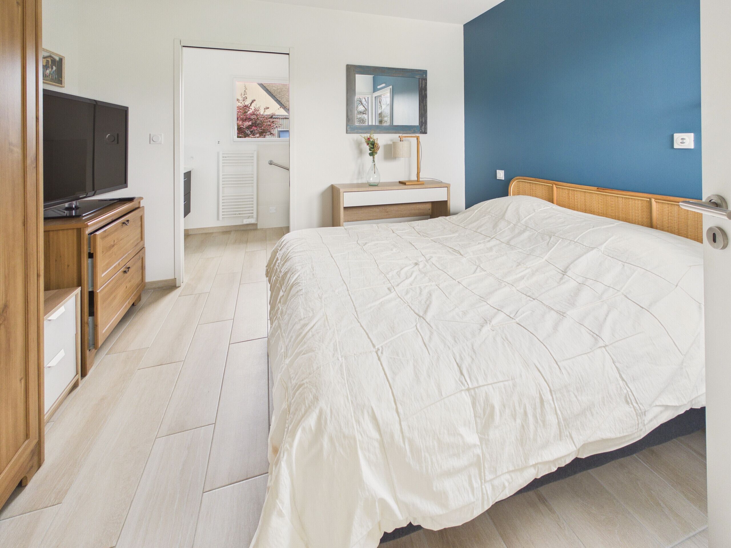 A bedroom with a bed, a TV, a dresser, a mirror, and a window.