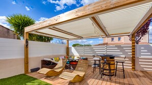 Een overdekte terras met houten ligbedden, een tafel en stoelen.