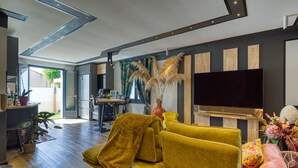 Een moderne woonkamer met een gele bank, een flatscreen televisie en een decoratieve plant.