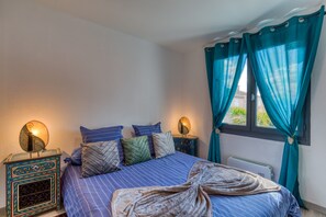 Ein Schlafzimmer mit einem Bett, Kissen, einem Nachttisch mit Lampe und Vorhängen.